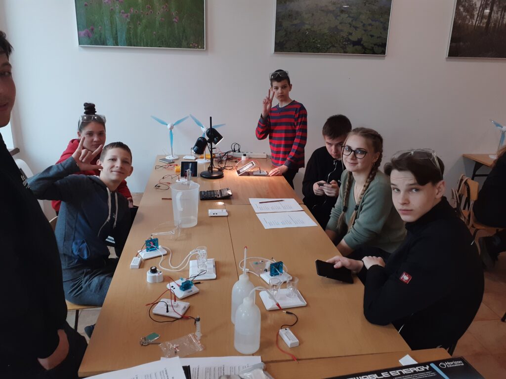 Grupa uczniów siedzących wkoło stołu patrzy się w stronę kamery 