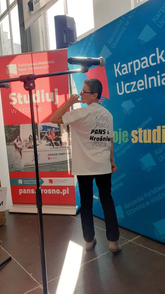 dr Marta Pisarek w koszulce X Targów Pracy, na tle bannerów promujących uczelnię PANS