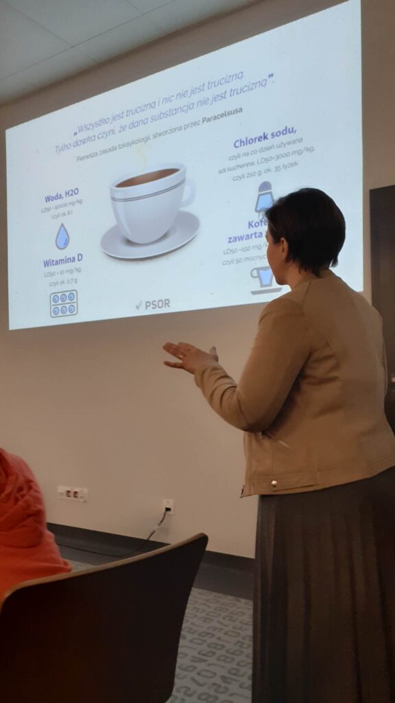 dr Joanna Gałązka podczas wykładu, slajd o znaczeniu szkodliwości lub jej braku w zależności od wielkości dawki